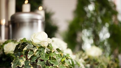 Nahaufnahme einer weißen Rose und Efeublättern auf einem Blumenarrangement mit Kerzen im Hintergrund.