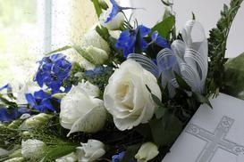 Blumenarrangement mit weißen Rosen und blauen Blüten, kombiniert mit einer tiefen Karte mit gekreuztem Motiv.