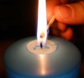 Nahaufnahme einer brennenden Kerze mit einer Hand, die ein Streichholz zur Flamme hält.