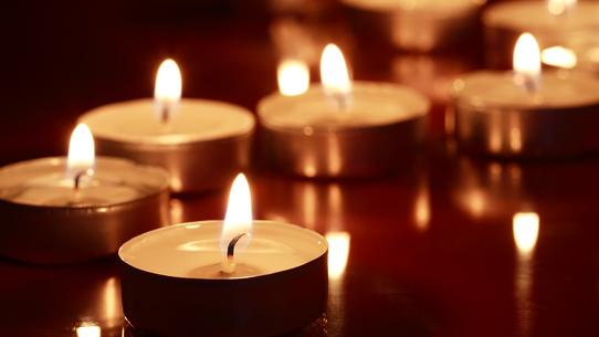 Eine Reihe brennender Teelichter auf einer reflektierenden Oberfläche in dunkler Umgebung.