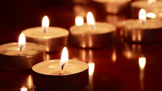 Eine Reihe brennender Teelichter auf einer reflektierenden Oberfläche in dunkler Umgebung.