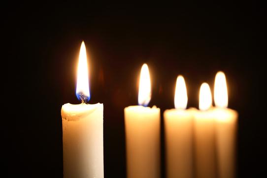 Nahaufnahme von fünf weißen Kerzen mit flackernden Flammen vor schwarzem Hintergrund.