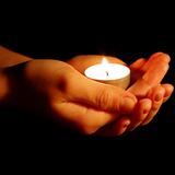 Hände halten eine flackernde Teelichtkerze vor einem dunklen Hintergrund.