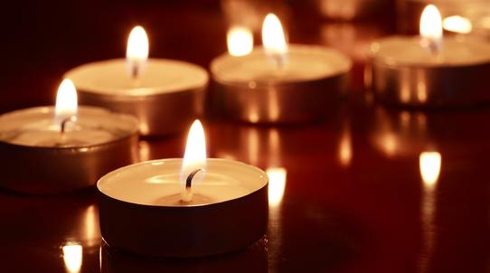 Eine Reihe brennender Teelichter auf einer reflektierenden Oberfläche in dunkler Umgebung.