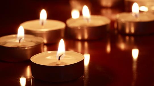 Eine Reihe brennender Teelichter auf einer reflektierenden Oberfläche in dunkler Umgebung.