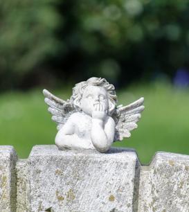 Skulptur eines nachdenklichen Engels mit kleinen Flügeln auf einem steinernen Untergrund im Freien.
