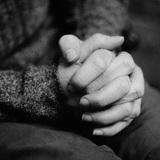 Nahaufnahme von zwei Händen, die ineinander verschränkt sind, vor einem unscharfen Hintergrund.